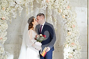 bride and groom kiss in an arch of flowers with a marriage certificate.