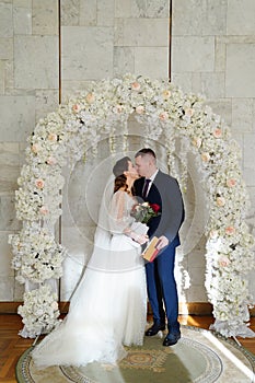 bride and groom kiss in an arch of flowers with a marriage certificate.