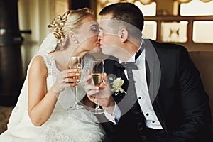 Bride and groom kiss holding wineglasses with champagne in their