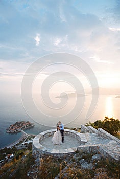 Bride and groom kiss on the observation deck over the Sveti Stefan island