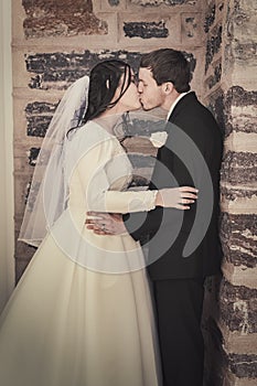 Bride and Groom Kissing by Brick Wall