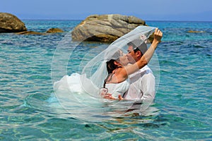 Bride & groom kissing in the clear blue sea water