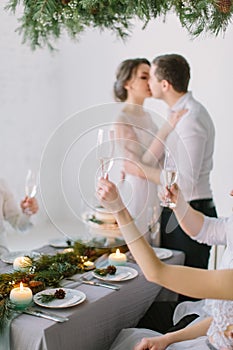 Bride And Groom kissing and Enjoying Meal At Wedding Reception. Guests drink champagne at the wedding table decorated