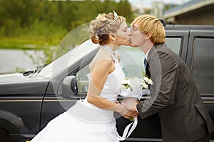 Bride and groom kissing near a car