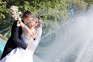 A bride and a groom kissing near the fountain