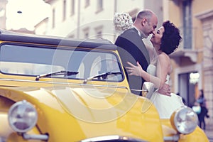 Bride and groom kissing near yellow car