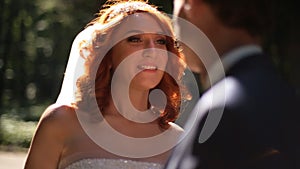 Bride and groom are kissing in a sunny park alley.