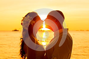 Bride and groom kissing on a tropical beach at sunset