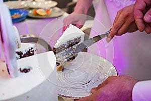 Bride and groom lay a cut piece of cake on a plate, bride and groom cut a wedding cake together