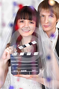 Bride and groom look; woman holds clapper board
