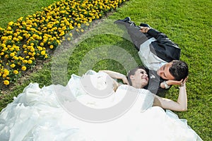 Bride and groom lying down on lawn with flowers