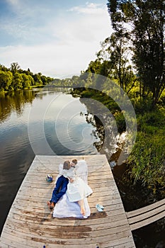 Bride and groom lying on a wooden pier near the pond