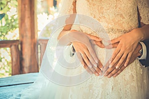 Bride and Groom make heart shape on bride`s belly as a symbol of love for the up coming baby