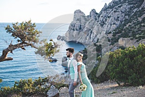 The bride and groom on nature in the mountains near the water. Suit and dress color Tiffany. Back to back.