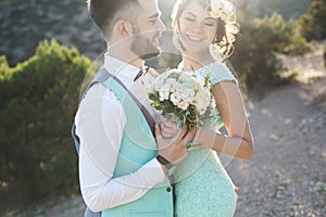 The bride and groom on nature in the mountains near the water. Suit and dress color Tiffany. Kiss and hug.