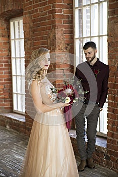 Bride and groom pose near window and vintage brick wall