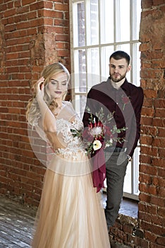 Bride and groom pose near window and vintage brick wall