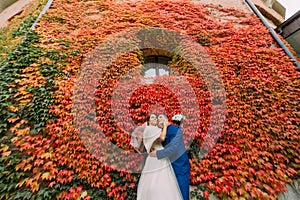 Bride and groom posing in park near fortified castle wall with red creeping plant