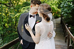 Bride and groom posing on the wooden bridge among greenery. Young people embrace each other and look at each other,happy