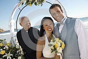 Bride and Groom with priest under archway