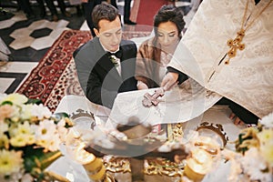 Bride and groom pronouncing vows, holding hands on bible on altar and priest holding golden cross on hands during holy matrimony photo