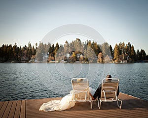 Bride and groom relaxing on lawn chairs on the dock looking out to the lake