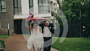 The bride and groom run in the rain, hiding behind a piece of tarpaulin. funny fun plan.