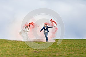 The bride and groom running through the field with red smoke bombs