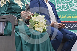 The bride and groom sit on chairs with their hands folded in prayer. Nikah is a Muslim wedding ceremony.