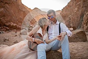 Bride and groom sit and hold hands in canyon. Closeup.