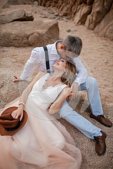 Bride and groom sit and smile on sand in canyon against background of rocks. Closeup.