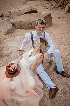 Bride and groom sit and smile on sand in canyon against background of rocks. Closeup.