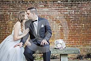 Bride and Groom sitting on bench in front of brick wall