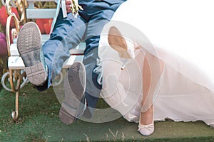 Bride and groom sitting on the bench, legs of bride and groom, black shoes, white heeled shoes