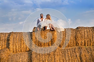 The bride and groom on the background of the sky are sitting on a large haystack