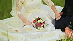 The bride and groom are sitting on green grass with a bouquet