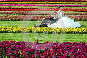 Bride and groom sitting on lawn with flowers