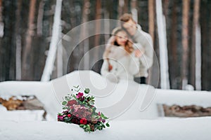 Bride and groom are sitting on the log in the winter forest. Close-up. Winter wedding. Soft focus on the bouquet