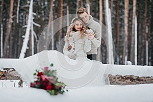 Bride and groom are sitting on the log in the winter forest. Close-up. Winter wedding. Soft focus on the couple