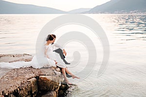 The bride and groom sitting on the pier and bride swinging her feet in the water