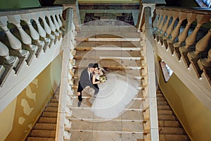 The bride and groom are sitting on a white marble staircase, holding hands and looking in the same direction