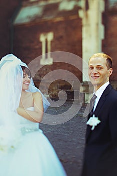 Bride and groom smile standing apart behind an old cathedral