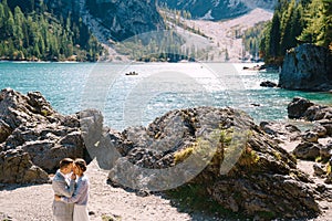 Bride and groom stand against the backdrop of stones overlooking Lago di Braies in Italy. Destination wedding in Europe