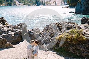 Bride and groom stand against the backdrop of stones overlooking Lago di Braies in Italy. Destination wedding in Europe