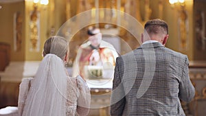 A bride and groom stand back to back in a Catholic church during their wedding.