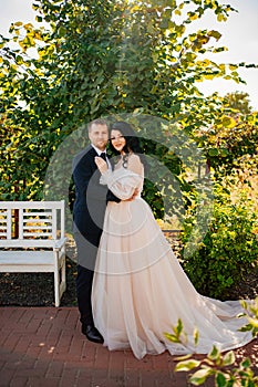 bride and groom stand by a bush with green foliage in the park.