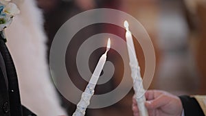 The bride and the groom stand in church, holding candles in their hands