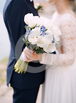 The bride and groom stand hugging and hold a wedding bouquet with white and blue flowers and eucalyptus branches close