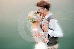 The bride and groom stand by the lake, after the wedding ceremony. Newlyweds are smiling, they are happy. Photo in warm tinting.