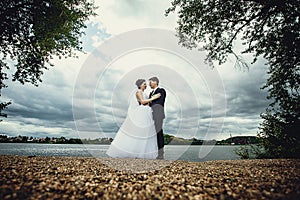 The bride and groom stand on the shore of the pond and look at each other. Beautiful full-length portrait